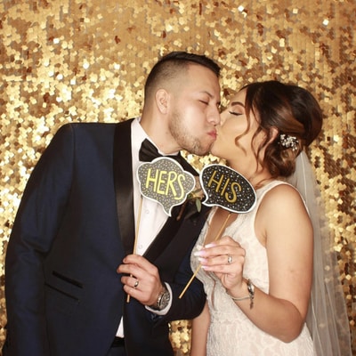 A newly wed couple taking a picture in front of a gold background while holding signs